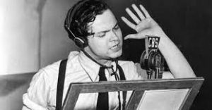 Orson Welles in front of the microphone, with raised hand, reading War of the Worlds
