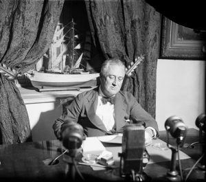 US president FD Roosevelt sitting at the desk, with radio microphone in front of him